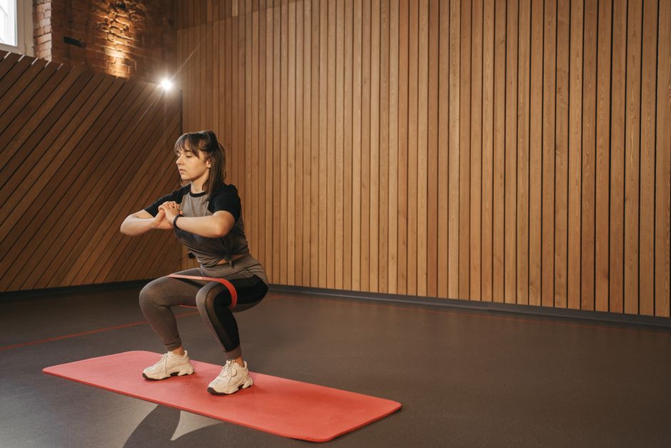 Young woman exercises indoors with resistance band on mat for fitness